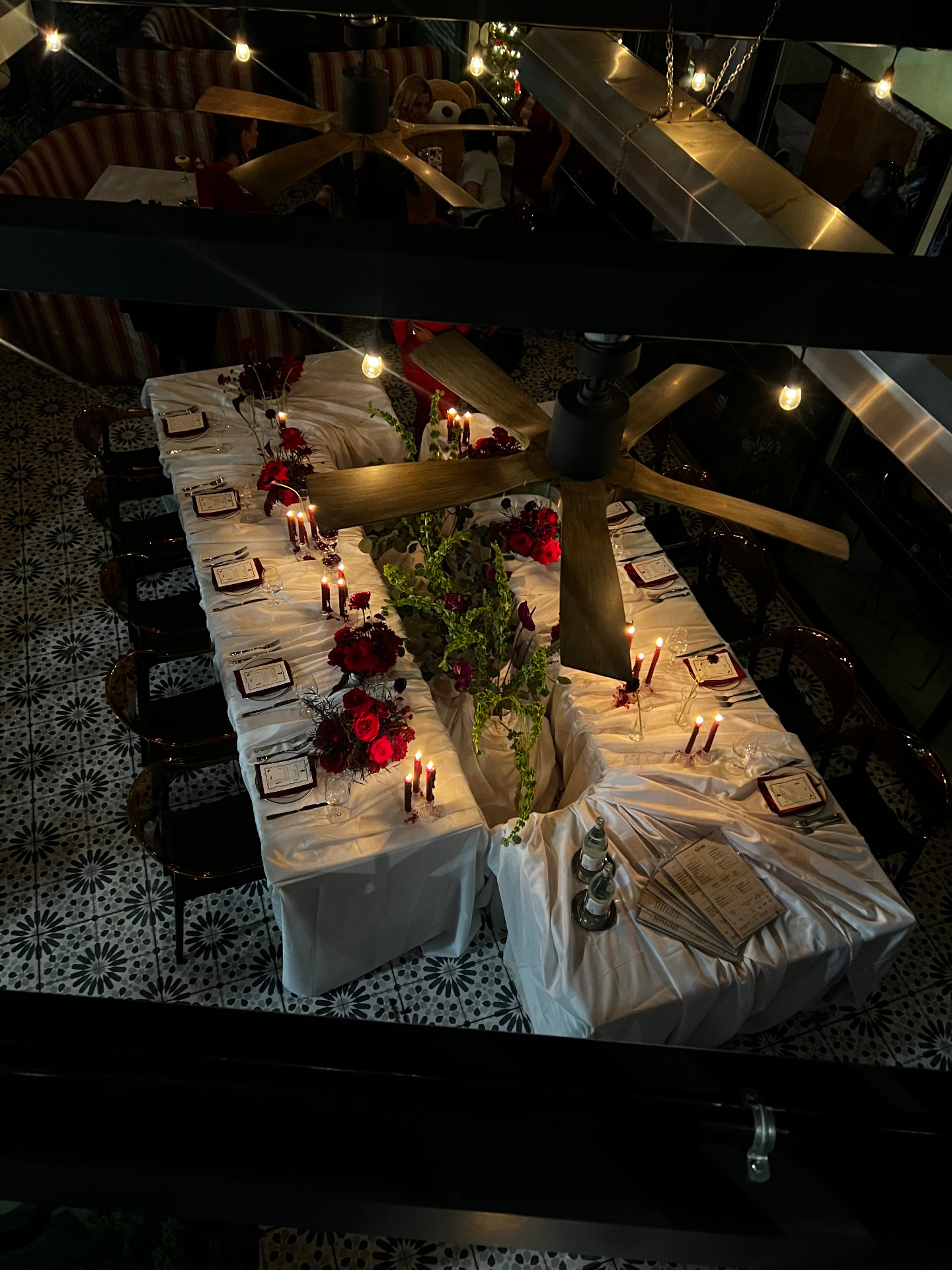 Overhead view of a long set dining table with red florals and lit burgundy candles