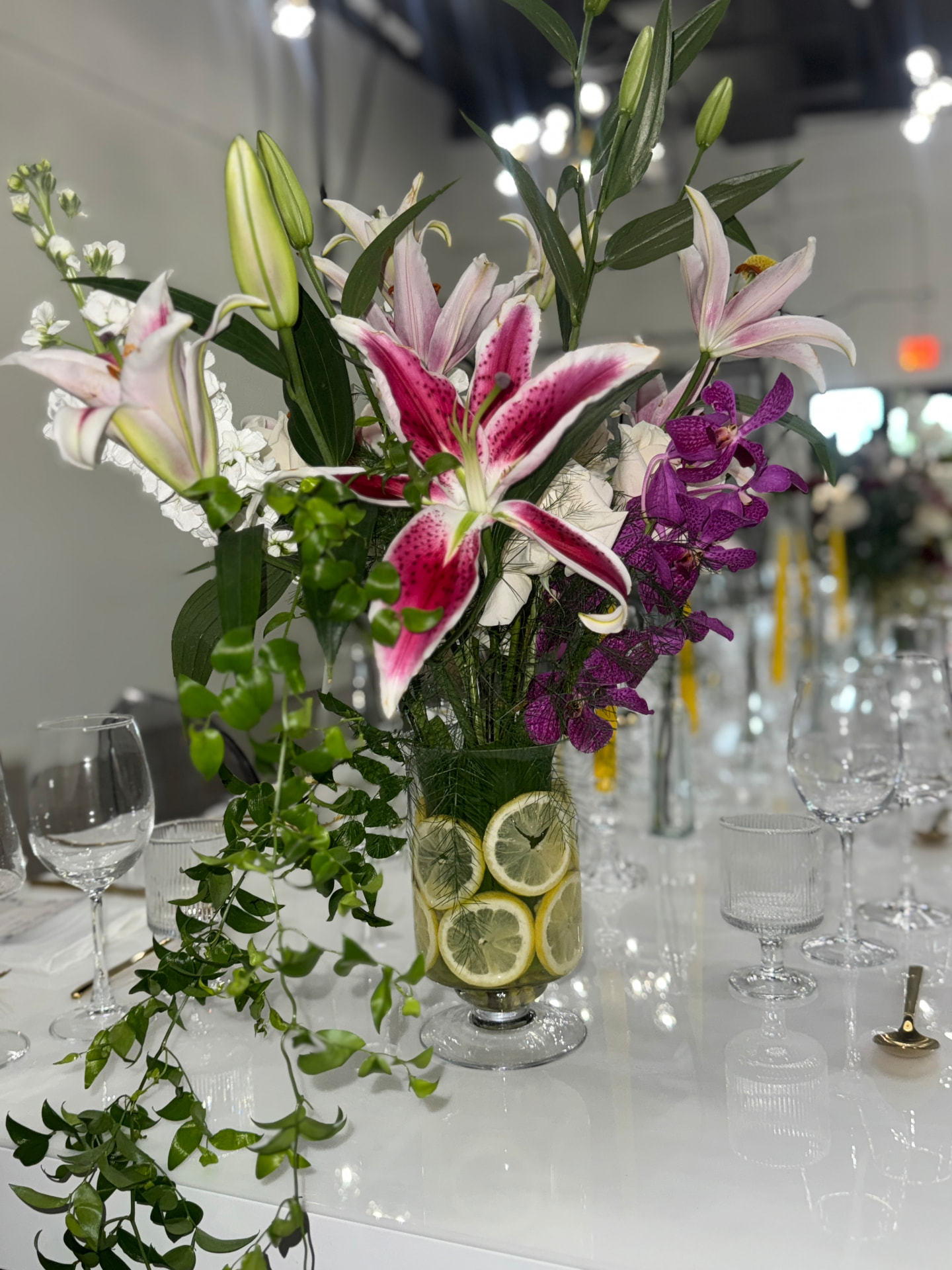 Floral arrangement of pink lilies and purple orchids in a lemon-lined glass vase