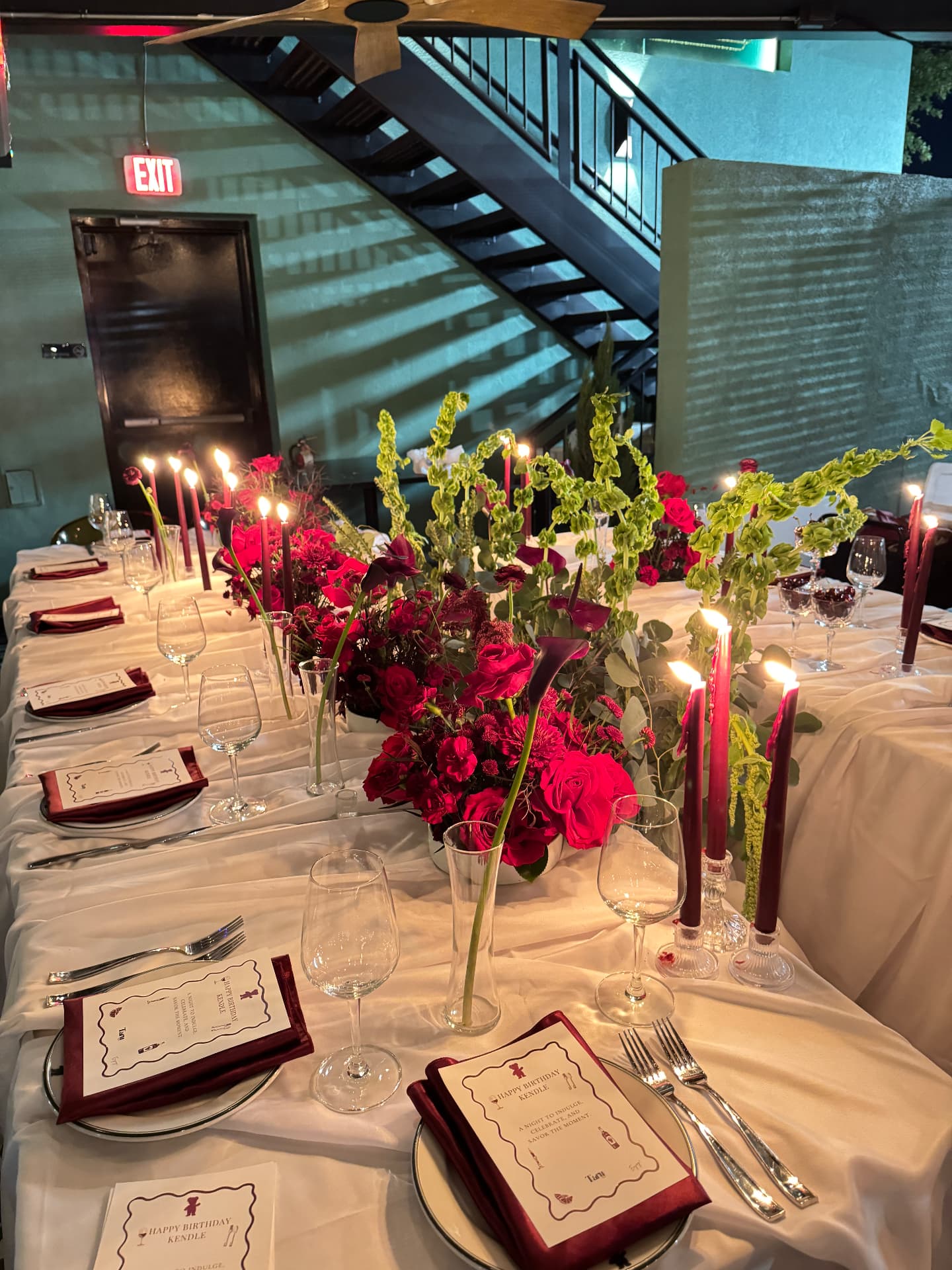 Birthday tablescape with red roses, foliage, and glowing burgundy candles