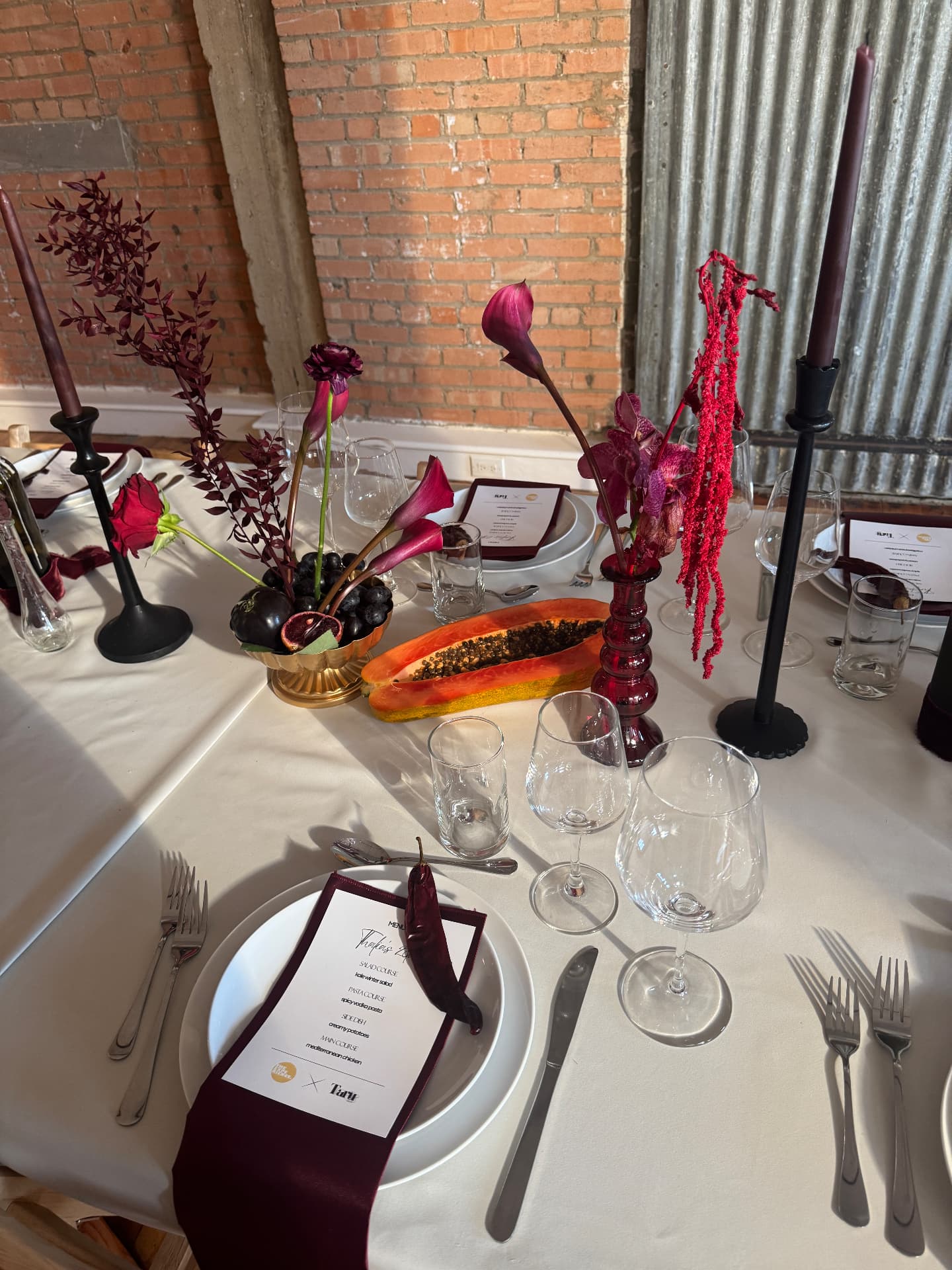 Top-down place setting with a maroon napkin, menu, halved papaya, and purple florals in a gold bowl