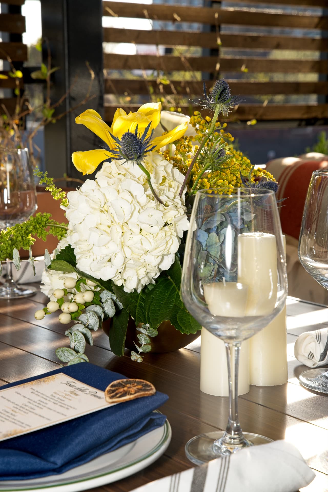 Sunlit tasting-dinner tablescape with navy menus, hydrangea, and candlelight