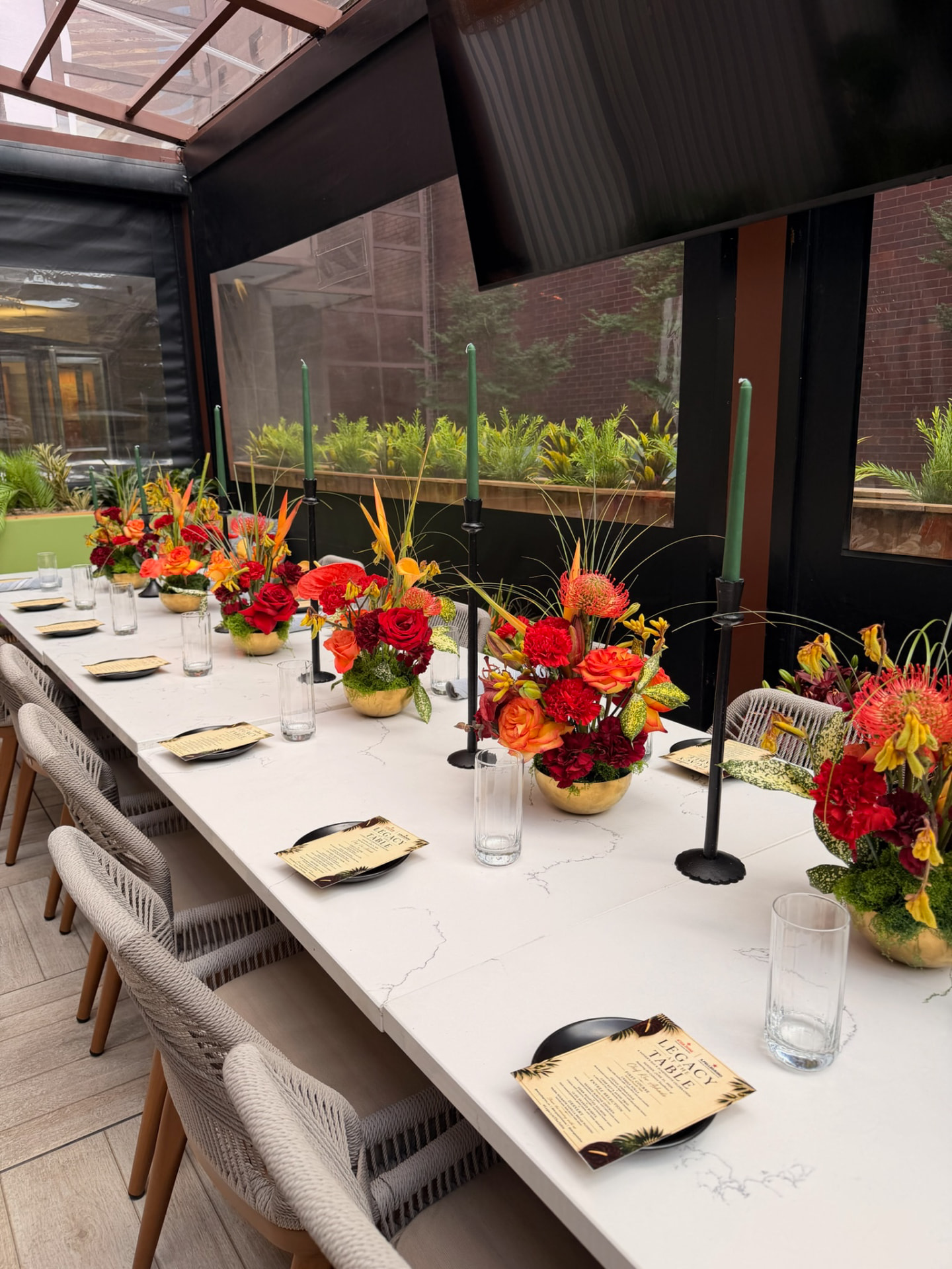 Long white marble table set with gold vessels of red and orange florals and green taper candles
